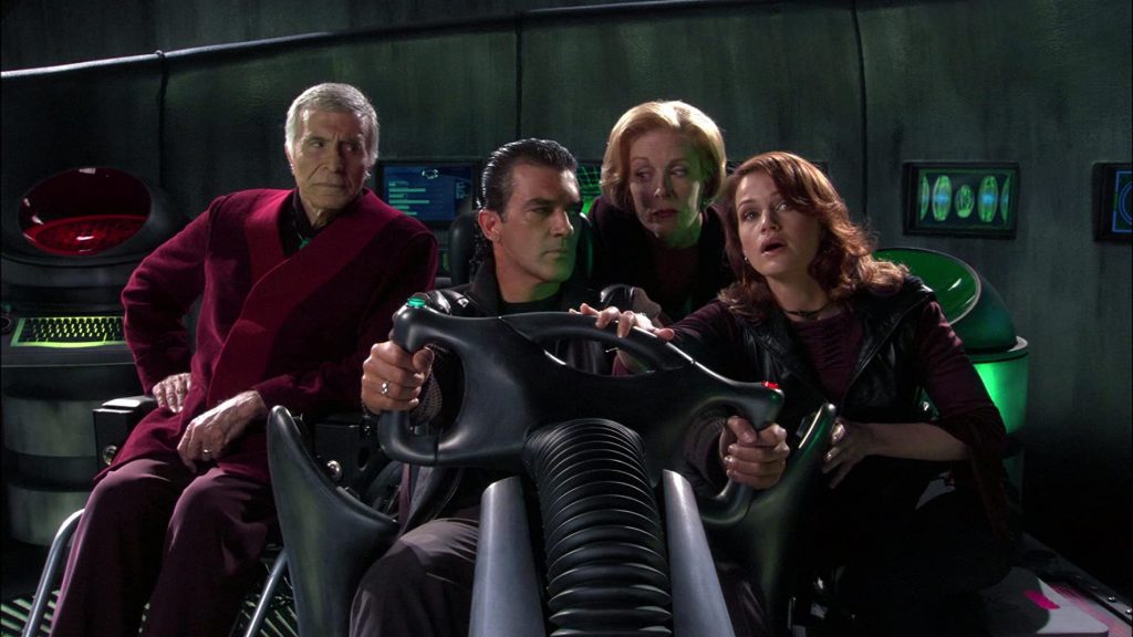 The parents and grandparents from the family in Spy Kids gathers around a huge steering wheel. The mom gently guides the dad's driving.
