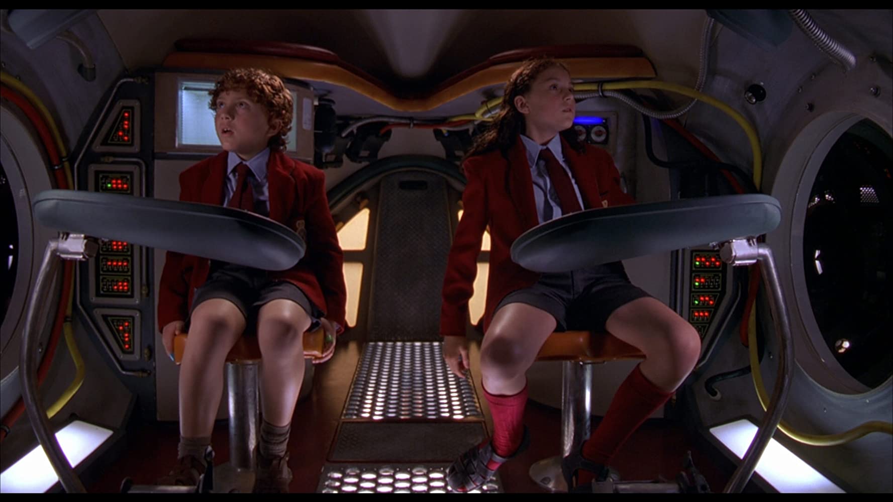 The brother and sister from Spy Kids, Carmen and Juni, sit inside a very weird vehicle, staring in amazement at the controls around them.